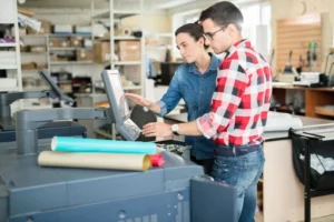 Two professionals collaborating over a large-format print in a modern office, showcasing the efficiency of outsourcing printing services.